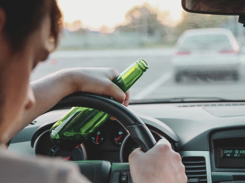 Drunk young man driving a car with a bottle of beer