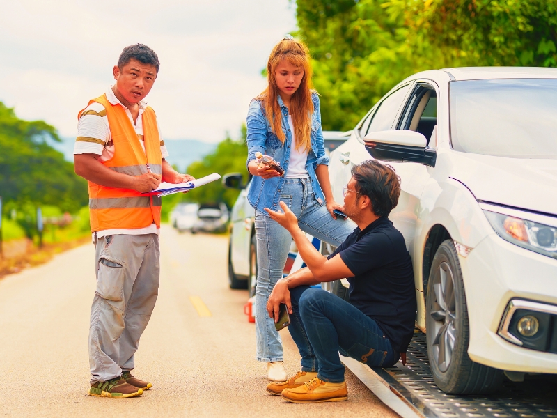 An insurance agent talks to a woman outside on the road after a car accident from drinking alcohol.