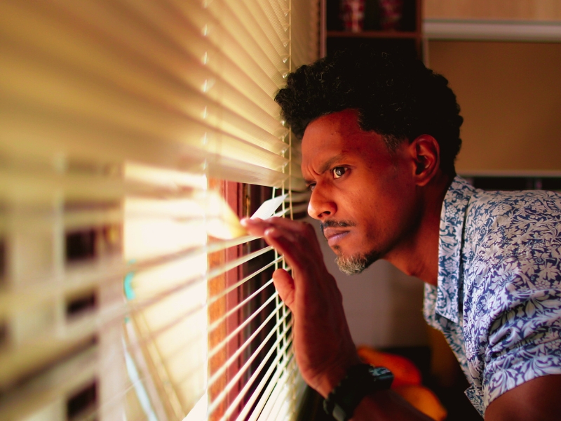 African man looking through window blinds