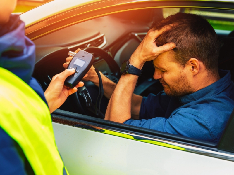 drink and drive concept - sad drunk man sitting in the car after police alcohol test with alcometer