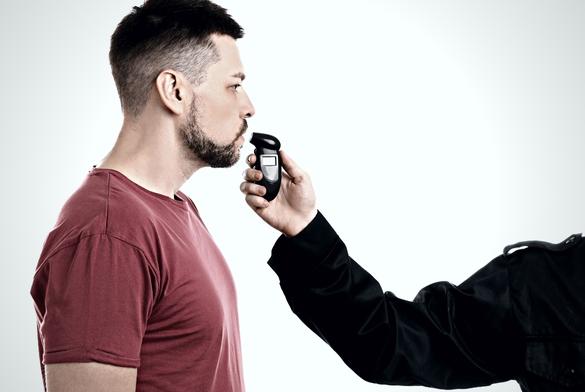 Police inspector conducting alcohol breathe testing, man blowing into breathalyzer on white background