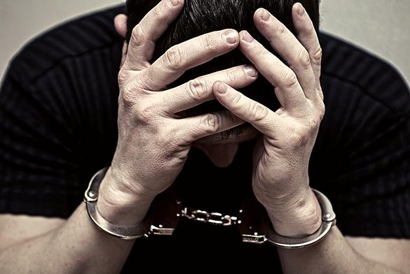 Handcuffed man covering his face with his hands.