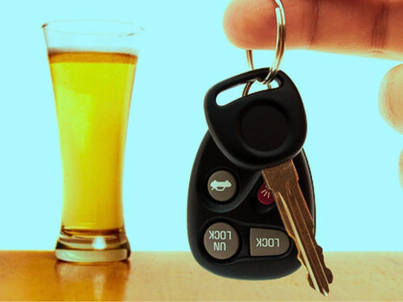 A glass of alcohol drink with a finger with car keys on the front.