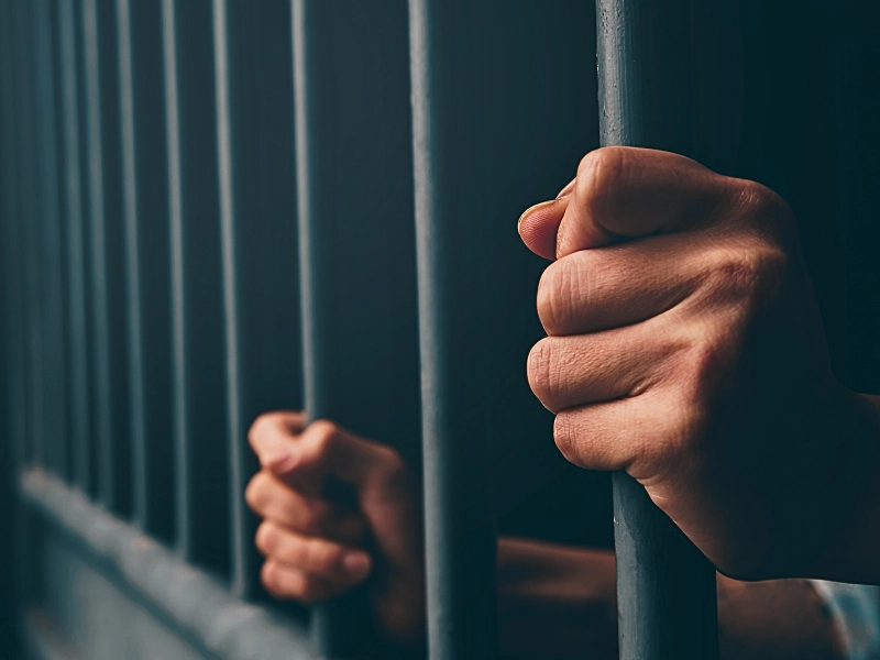 Man in prison hands of behind hold Steel cage jail bars.