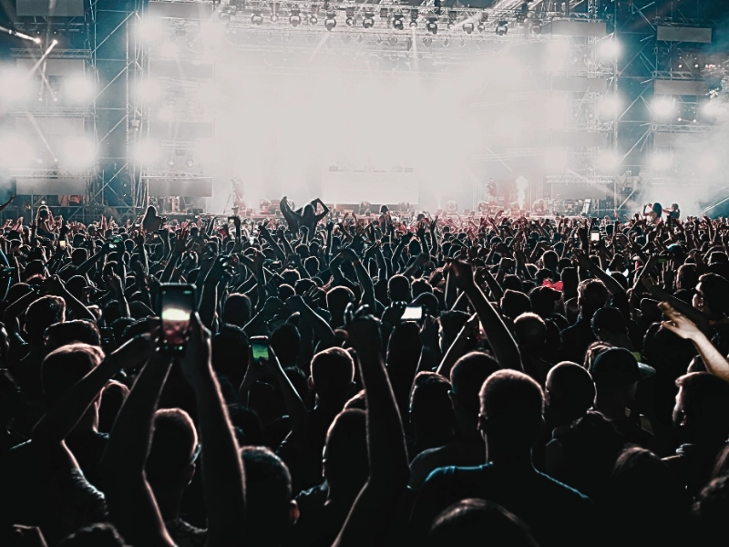 Back view of excited audience with arms raised cheering in front of the stage at music. Caught With Club Drugs