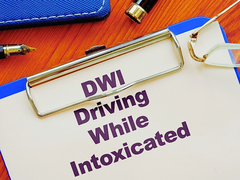 DWI driving while intoxicated printed on a paper clipped on a board with open fountain pen on a wooden table. DWI While Riding a Scooter
