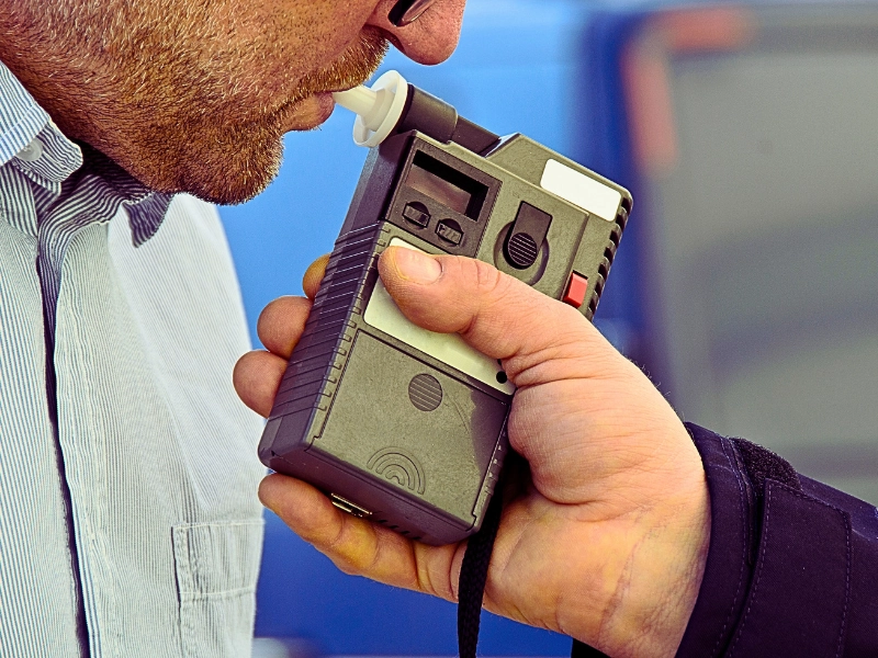 a person blowing into a handheld breathalyzer device, which is being held by another individual.
