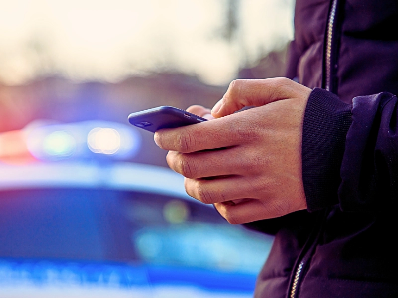 Person using smartphone with blurred police lights background. charged with a drug crime based on text messages